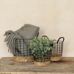 two baskets with plants in them sitting on a wooden table next to a gray blanket