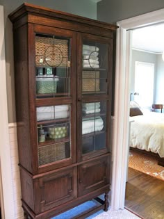 a wooden cabinet with glass doors and baskets on the bottom shelf in a room that has hardwood floors