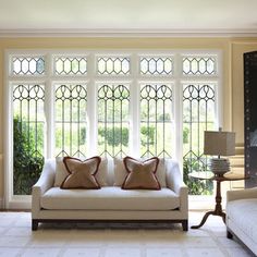 a living room with two couches and a table in front of large windows that have stained glass panes on them