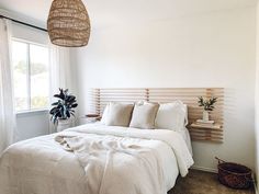 a bed with white linens and pillows in a bedroom next to a plant on the wall