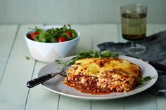 a white plate topped with lasagna next to a bowl of salad