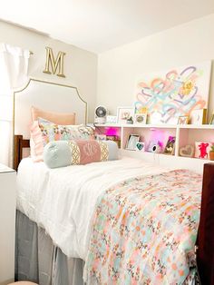 a white bed topped with lots of pillows next to a shelf filled with pictures and other items