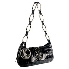 From the Spring/Summer 2005 collection, this black patent leather Yves Saint Laurent shoulder bag, designed by Stefano Pilati, features silver-tone hardware, small front pockets, and a 'YSL' branded charm. The same style appeared in the season's ad campaign shot by Juergen Teller and modeled by Karen Elson. The bag draws inspiration from Yves Saint Laurent's Spring 1969 'Safari' collection, with a shoulder strap made of metal rings and a tie-accented flap, both elements reinterpreted from the or Stefano Pilati, Y2k Shoulder Bag, Juergen Teller, Karen Elson, Pink Fruit, Dolce And Gabbana Blue, Drawing Bag, Sunglasses Logo, Ysl Logo