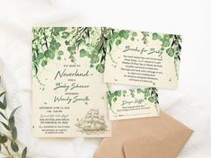 the wedding stationery is laid out on a white blanket with greenery and leaves