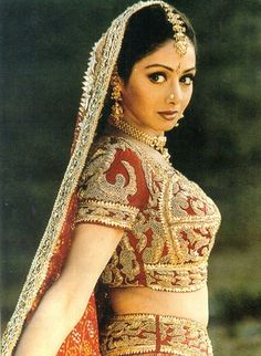 a woman in a red and gold bridal outfit with her hand on her hip