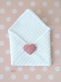 a white crocheted envelope with a pink heart on the front and bottom, sitting on a polka dot background