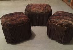 three stools made out of cowhide with fringed edges and studding on them