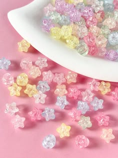 small multicolored beads are scattered on a pink surface next to a white bowl