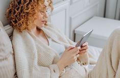 a woman sitting on a bed looking at her cell phone while she is using it