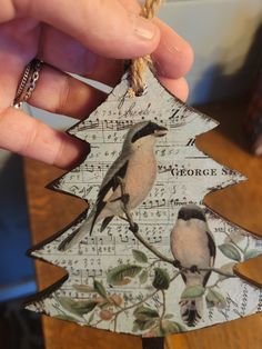 a hand holding a piece of paper with a bird on it and music notes hanging from the tree