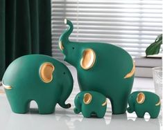 three green elephants standing next to each other on a white table with curtains in the background