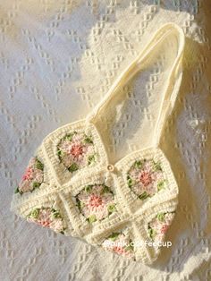 a crocheted purse sitting on top of a white tablecloth covered in pink and green flowers