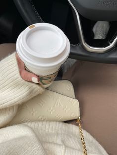 a woman holding a cup of coffee in her hand while sitting in a car seat