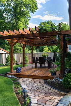 Wooden pergola on a backyard deck with outdoor dining set. Paved pathway leads to the deck, surrounded by lush greenery and decorative plants. Back Porch With Pergola, Decks With Pergolas And Fire Pit, Landscaping Around Pergola, Pergola And Deck, Pergola Off The House, Wood Deck With Pergola, Pergola Accessories Outdoor, Shade Structure Backyard, Garden Living Room Outdoor