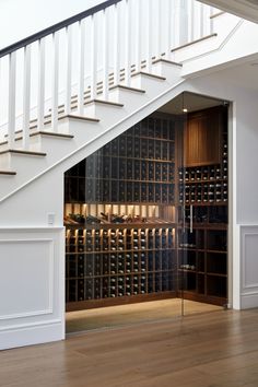 an open wine cellar under the stairs in a room with wooden floors and white railings