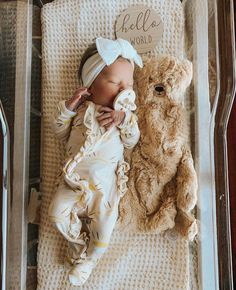 a baby laying next to a teddy bear in a clear box with hello world written on it