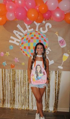 a young woman standing in front of a backdrop with balloons and an image on it