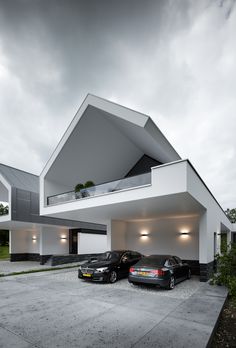 two cars are parked in front of a modern house with an angled roof and white walls