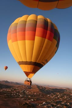 two hot air balloons flying in the sky over a small town and desert area with houses