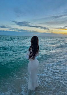 a woman standing in the ocean at sunset with her back to the camera, looking into the distance