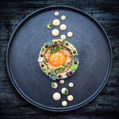 a black plate topped with food and garnishes on top of a wooden table