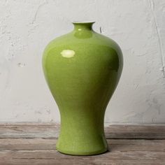 a large green vase sitting on top of a wooden table next to a white wall