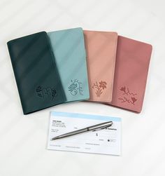 four different colored notebooks and a pen on top of a white table with a check card