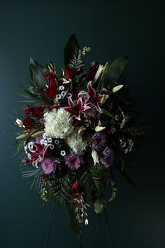 a bouquet of flowers on a stand against a green wall with leaves and other foliage