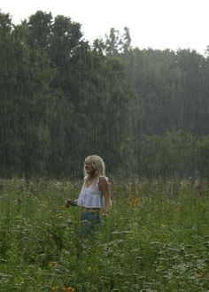 a woman standing in the middle of a field with an umbrella over her head and trees behind her