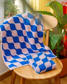 a blue and white blanket sitting on top of a wooden chair next to a potted plant