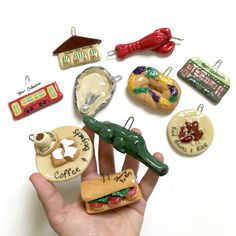 a hand is holding a miniature sandwich and some other items in the shape of magnets