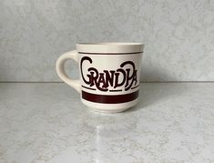 a coffee cup sitting on top of a counter next to a white wall with the word grandpa written on it