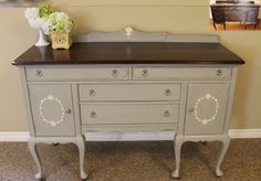 an antique dresser painted in gray with white trim and flowers on the top, against a beige wall