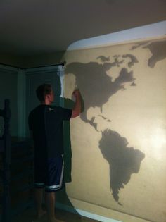 a man standing in front of a wall that has a map on it with the shadow of the world on it