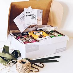 an open box filled with lots of different items next to a ribbon and some scissors