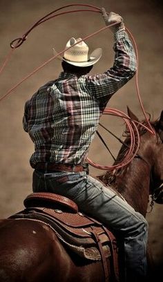 a man riding on the back of a brown horse wearing a cowboy hat and lasso