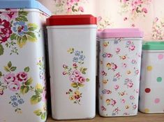 four flowered canisters are lined up on the shelf next to each other