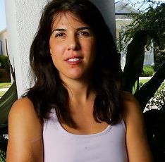 a woman in a tank top sitting on a porch next to a tree and house