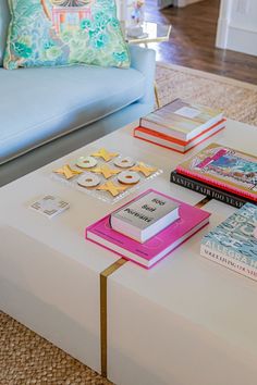 a coffee table topped with lots of books on top of a white ottoman next to a blue couch