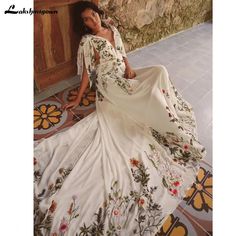 a woman is sitting on the floor in a long white dress with flowers and leaves