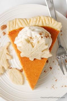 a slice of pumpkin pie on a white plate with whipped cream and leaves around it