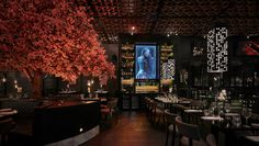 a dimly lit restaurant with tables, chairs and trees in blooming red leaves on the ceiling