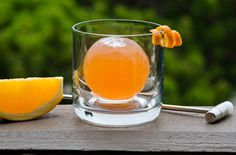 an orange sitting on top of a wooden table next to a glass filled with liquid