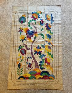 a quilt hanging on the wall with an image of a tree and flowers painted on it