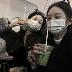 two women wearing face masks and drinking starbucks coffee on an airplane with straws in their hands