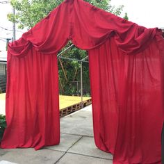 an open red curtain on the side of a building next to a wooden platform and trees