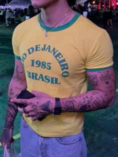 a man with tattoos on his arm holding a cell phone and wearing a yellow shirt