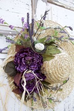 a straw hat with purple flowers and an easter egg on the top is hanging from a wall