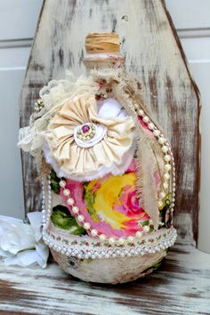 an old bottle is decorated with flowers and pearls on the top, sitting on a wooden chair