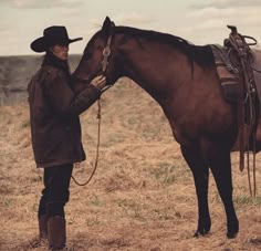 a man standing next to a brown horse on top of a dry grass covered field